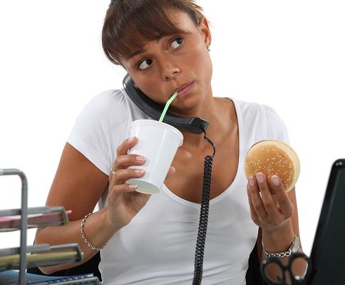 young woman eating hamburger and drinking out of a straw while making a call