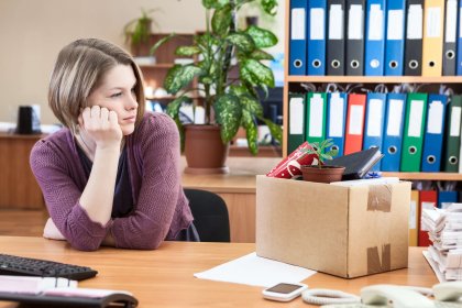 Young worker with regret looking at box with personal belongings on table